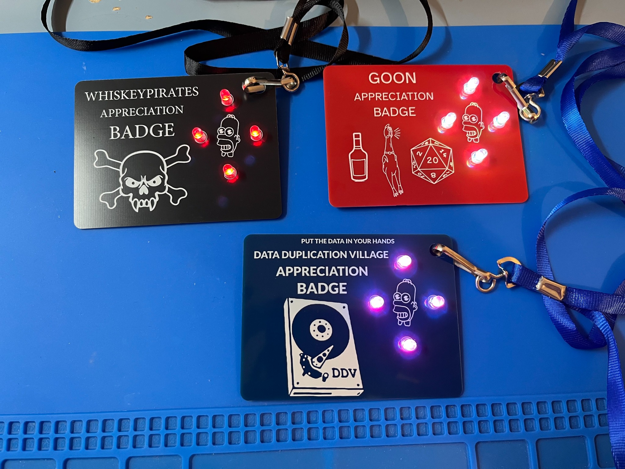 Three finished DEF CON 34 PCB appreciation badges for Whiskey Pirates, Goons, and the Data Duplication Village